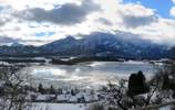 Foto: Blick vom Enzensberg auf den aufbrechenden Hopfensee. 
Über die Berge im Hintergrund fegen wilde Wolkenfetzen