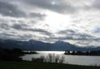 Foto: gekräuselter, glitzernder Forggensee vor Schneebergen, strukturierte Wolken