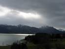 Foto: Blick über den Forggensee zum Tegelberg - das Wasser glitzert, die Wolken ziehen düster