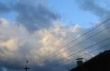 Foto: Vogel landet auf Draht. Aufgetürmte, zerrissene Wolken